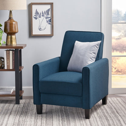 Blue armchair with a gray pillow in a room with a side table and framed artwork.