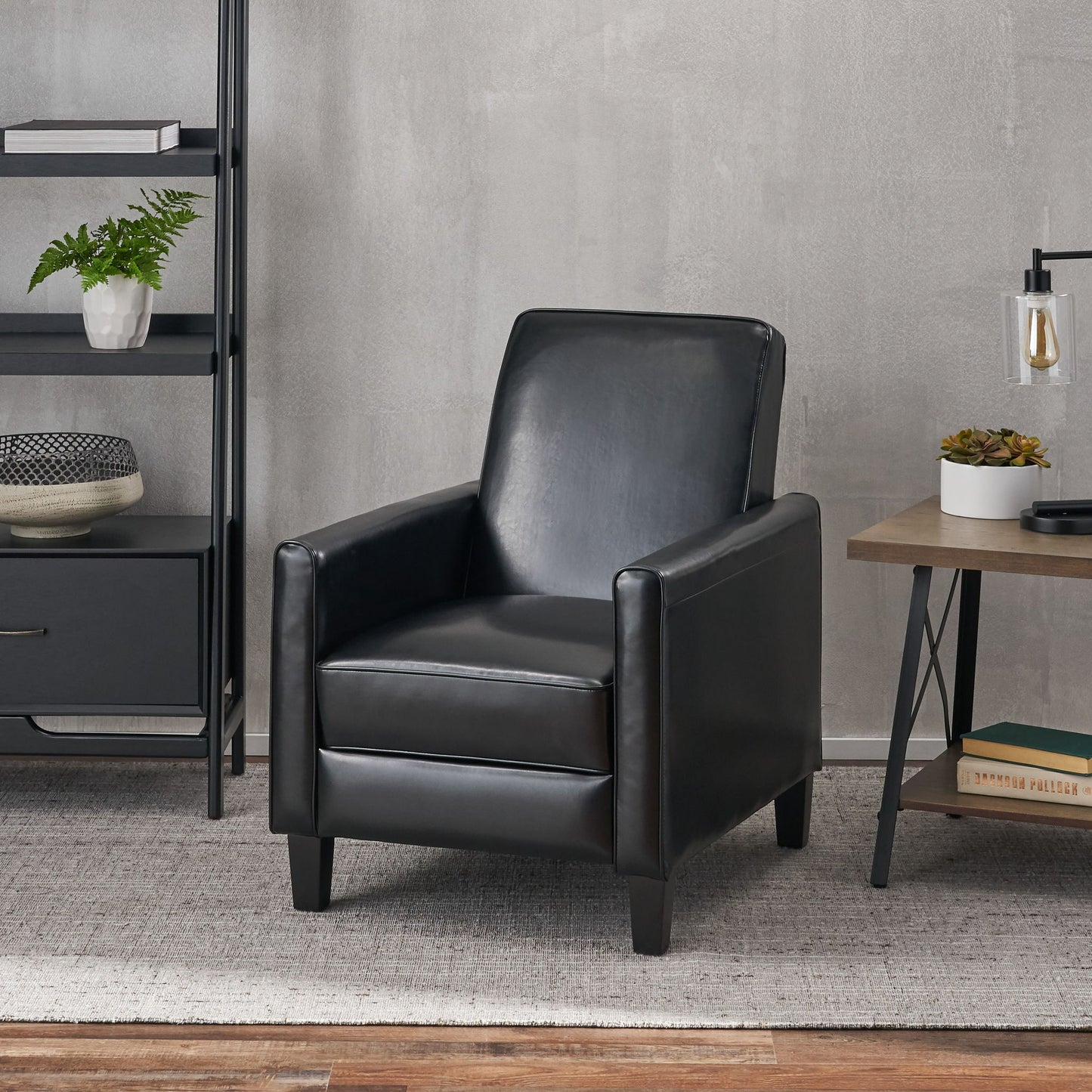 Black leather armchair in a modern living room setting with a gray wall and wooden floor.