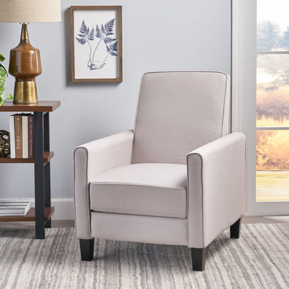 Gray armchair in a room with a lamp, books, and a framed picture on the wall.